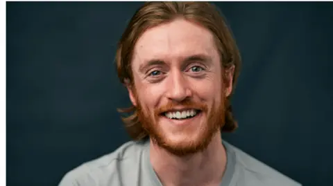 Michael Hawkins Michael Hawkins, who has red hair and a red beard and blue eyes, smiles at the camera.