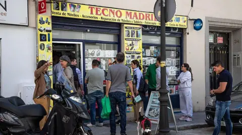 Bloomberg via Getty Images Customers queue outside a shop selling tech devices including power banks during a power outage in Madrid, Spain