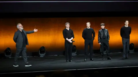Reuters Paul Mescal, Joseph Quinn, Barry Keoghan and Harris Dickinson stand on a stage, with Sam Mendes to the left, extending his arm as he presents them to the audience at a press conference to launch his four-part Beatles biopic