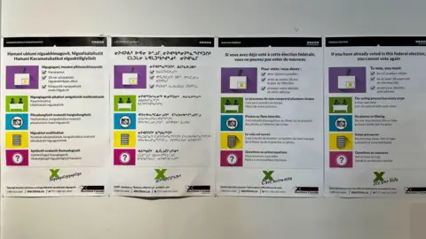 Jean-Claude Nguyen Election instructions in English, French and Inuktitut hanging on a wall