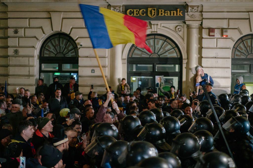Crowd of protestors clashes with police, a protestor carries a Romanian flag
