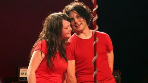 Getty Images Jack and Meg White smile and hold hands during a concert
