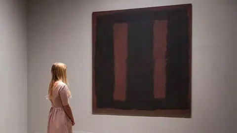 Getty Images A woman in a pink dress looks at Mark Rothko's painting Black On Maroon 1958, a painting of two maroon strips on a black background, after it went back on display at Tate Modern gallery