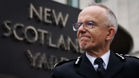Getty Images Commissioner Sir Mark Rowley stands in front of the New Scotland Yard sign, looking to the side with a serious expression