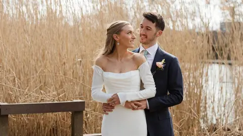 Rosie Davison Photography Ellie and her husband stand together in their wedding outfits on their wedding day, holding hands and staring into each other's eyes