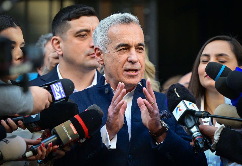 Politician Calin Georgescu speak, surrounded by press microphones.