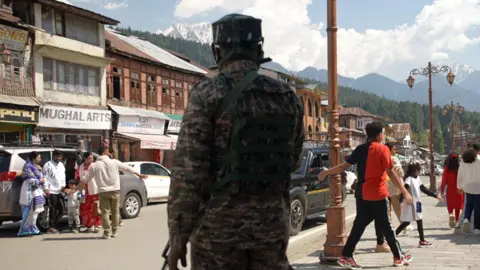 Seraj Ali The image shows the main high street in Pahalgam with a few tourists as well as a security personnel in uniform, carrying a gun.