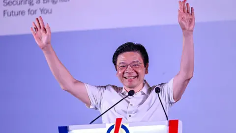 Getty Images Singapore PM Lawrence Wong smiles with both his arms held aloft as he addresses a crowd at an election rally