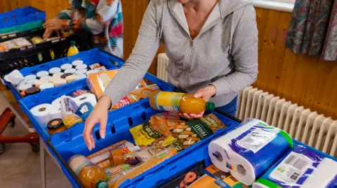 Getty Images A volunteer sorts food and household supplies into crates at a food bank