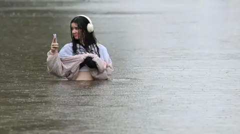 Getty Images A woman stands waist deep in a flood in a suburb of Brisbane in March