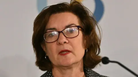 Getty Images Close up image of Eluned Morgan talking at a government event. She is talking whilst looking out at the audience. She has brown short hair and is wearing glasses.