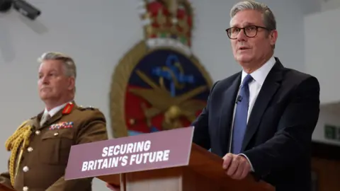 EPA UK Prime Minister Keir Starmer in a suit, accompanied by General Sir Jim Hockenhull in military uniform standing at podiums with a sign that reads 'Securing Britain's Future'