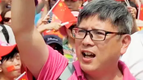 Innes Tang Innes Tang at a pro-Beijing rally - he is wearing a pink shirt and has his arm raised aloft. Many people are in the background waving Chinese flags