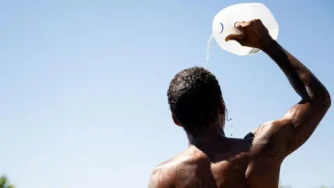 Getty Images A man pours water from a large container on his head on a sunny day.