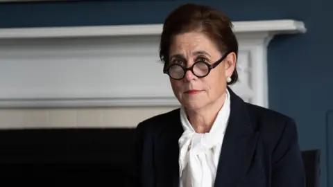 PA Media Baroness Lampard sits in the inquiry office at Arundel House in London. She is wearing a white shirt and navy suit. Her glasses are rounded and tortoiseshell in colour and she is looking direct at the camera with her hair up. She is wearing pearl earrings.