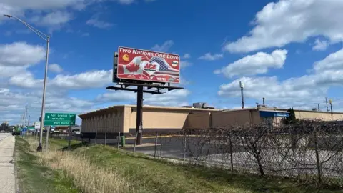 Billboard with two hands making a heart, one hand has the Canadian flag and the other has the American flag. The sign reads