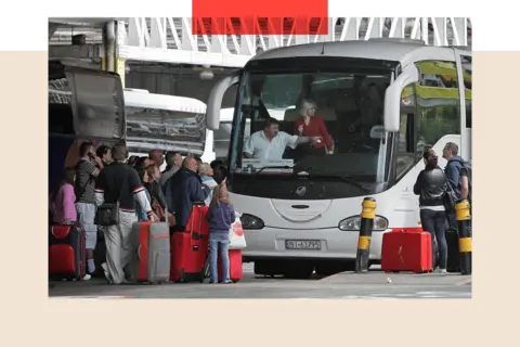 Getty A bunch of people queue up to get on a white coach. Most of the people have red suitcases.