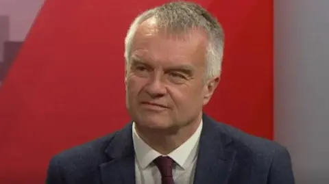 Reform UK's West Midlands regional director Pete Durnell, looks to the left, in the BBC Politics Midlands studio - he is wearing a white shirt, dark tie and suit