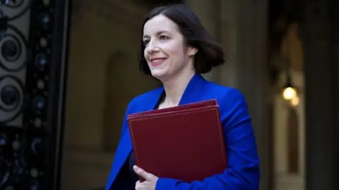 PA Media Bridget Phillipson smiling, wearing a blue suit and carrying a dark red folder