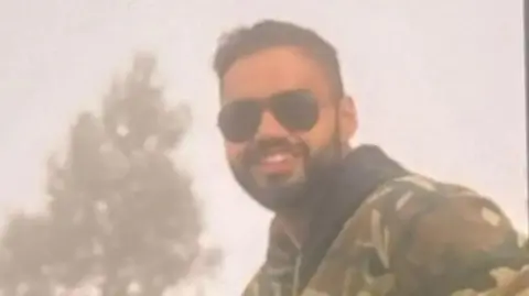 Kamal Saini/BBC The photograph shows a bearded man, Vinay Narwal, wearing black sunglasses and a green camouflage jacket and posing for the camera