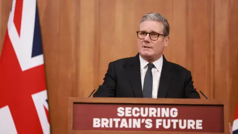 PA Media Prime Minister Sir Keir Starmer, wearing a dark suit and tie, speaks behind a lectern displaying the phrase Securing Britain's Future during a press conference on the Immigration White Paper in the Downing Street Briefing Room in London.
