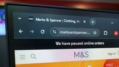 A close-up photo of the Marks and Spencer website shows a black banner with white font informing visitors:
