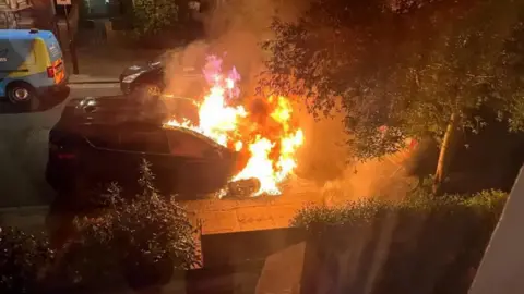 SUPPLIED The front half of a car parked on a residential street is seen engulfed in flames.