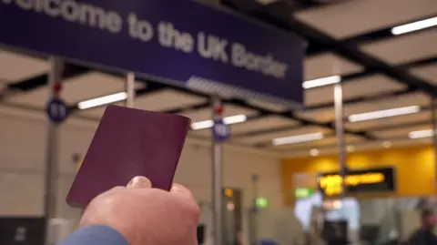 BBC Man holds up passport with e-gates in background