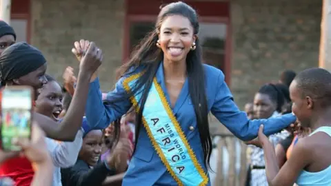 Lesego Chombo/Instagram Lesego Chombo in a blue suit with a Miss World Africa sash bhold the hands of young girls
