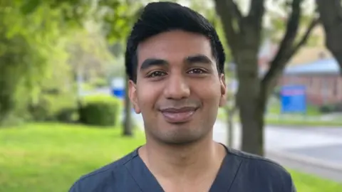 Samren Reddy stands in grounds with grass and trees behind him.