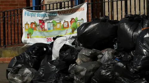Reuters Bin bags are stacked up in a heap next to a community sign that reads 