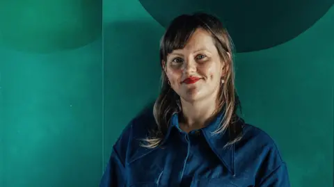 Taran Wilkhu Sabine Zetteler in a blue shirt against a green background
